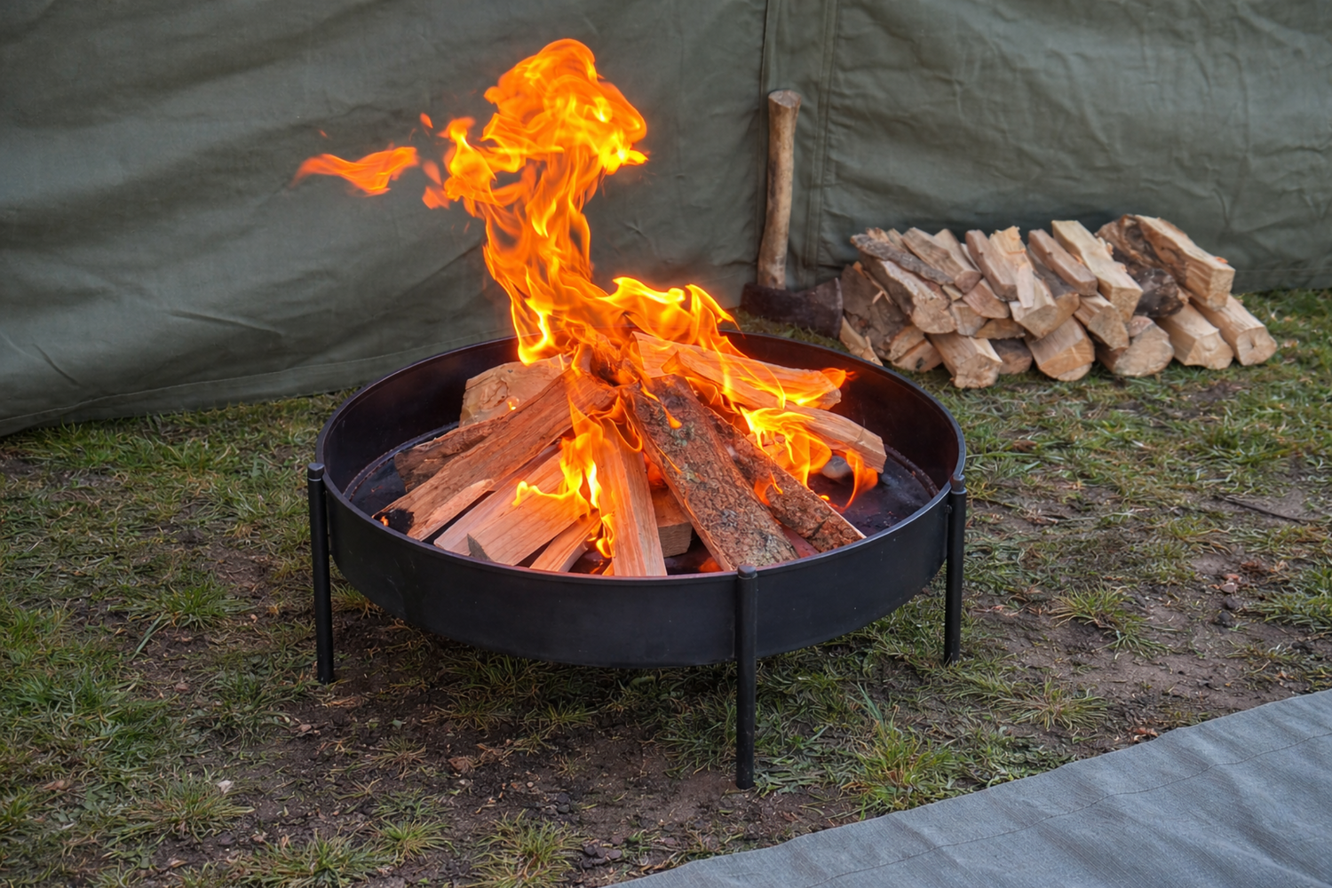 Round metal fire pit with burning logs outdoors on grass