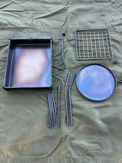 Collection of metal kitchen utensils including a grill, strainer, and skewers on a beige fabric background.