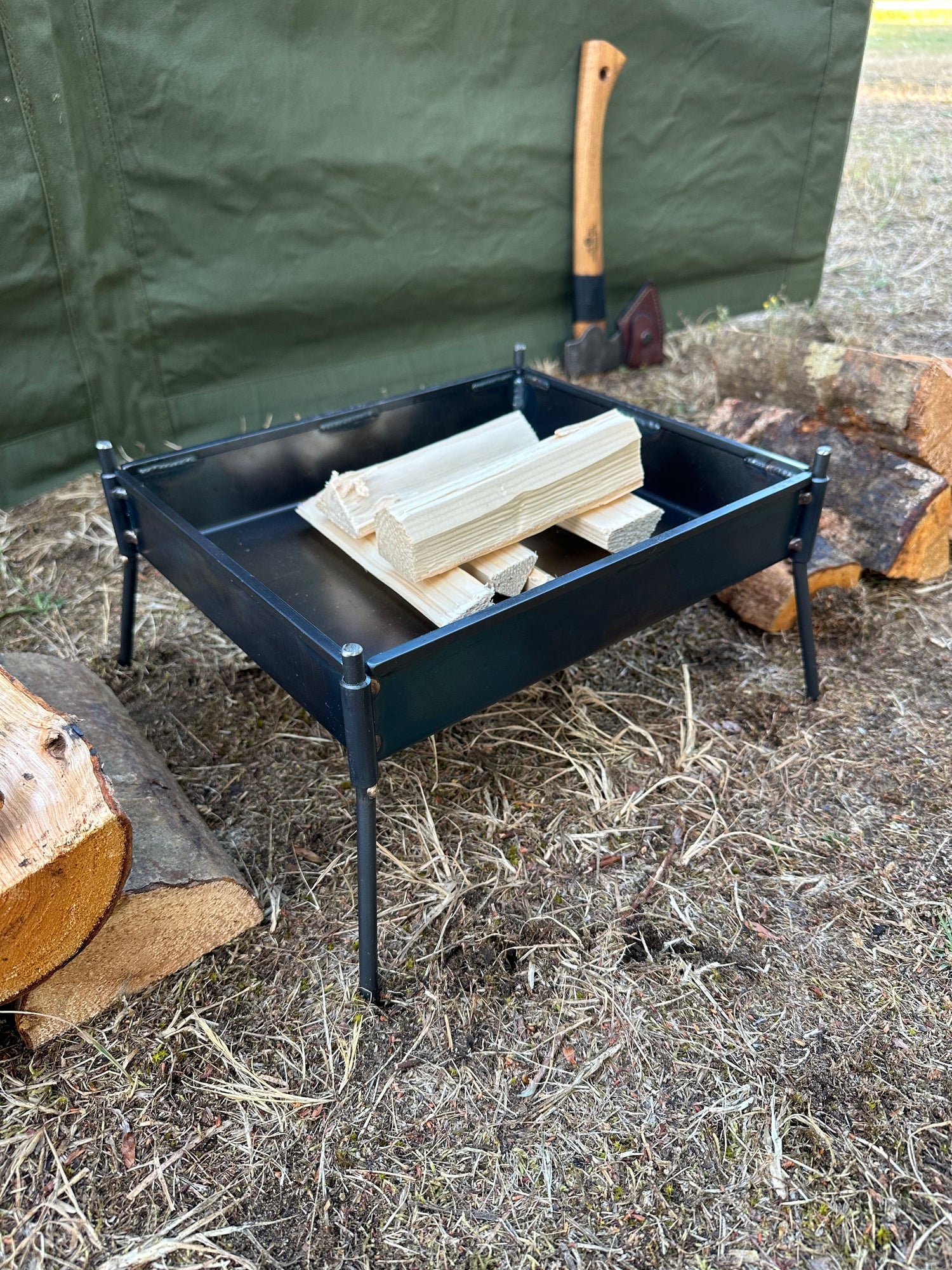 Black metal fire pit with wooden logs on a grassy ground