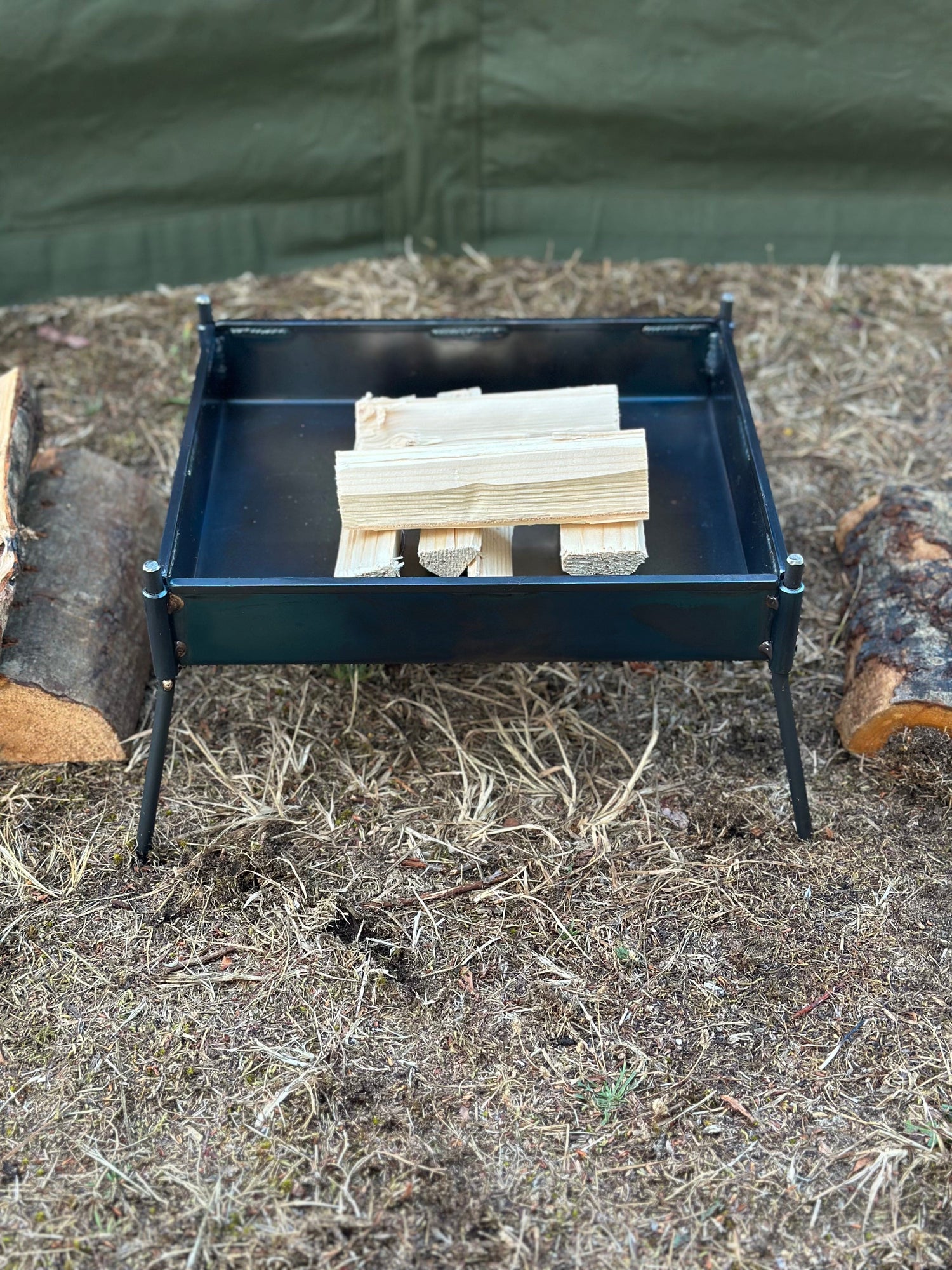 Small black metal grill with wooden sticks on a grassy ground.