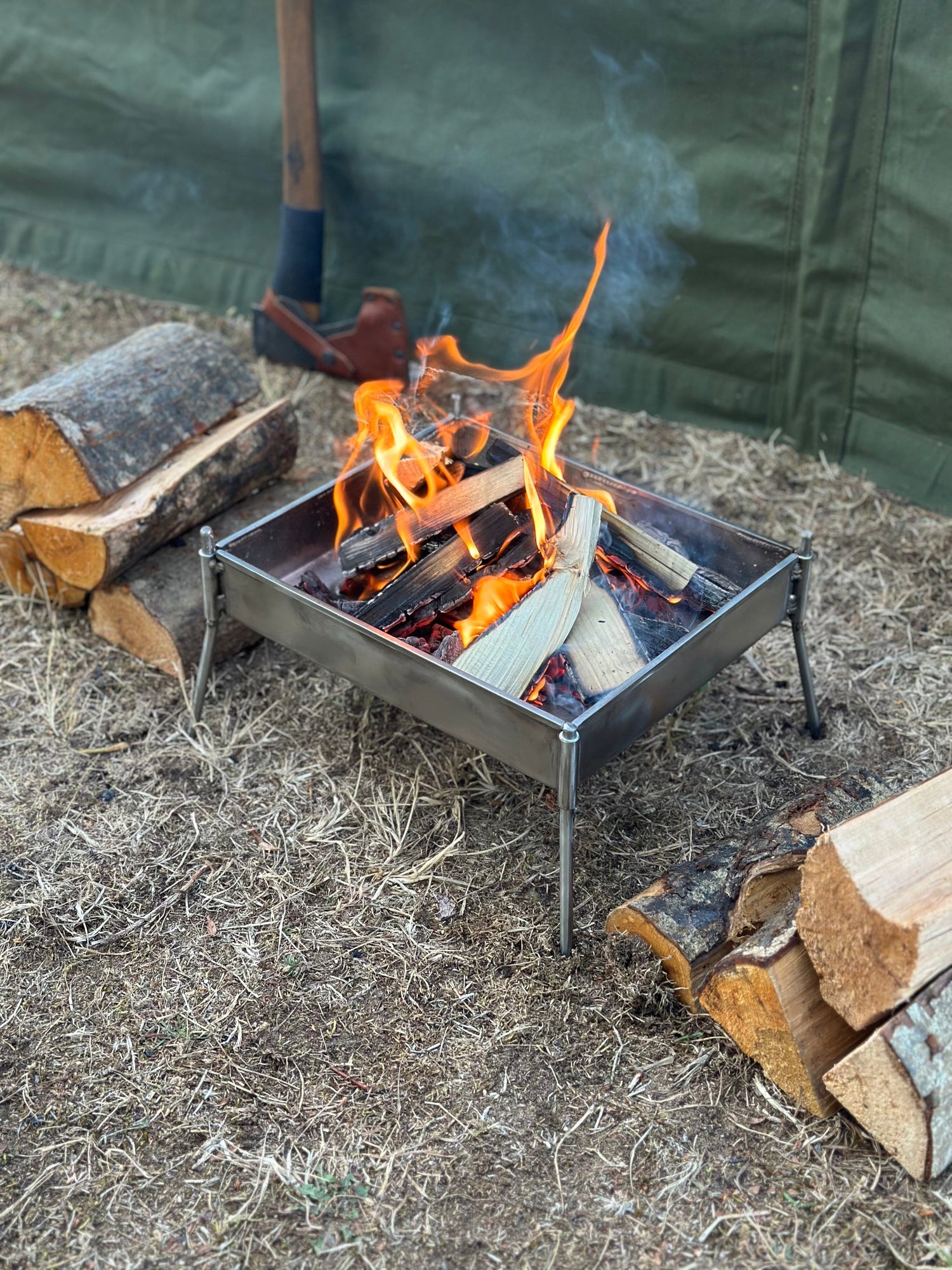 Small metal fire pit with flames and logs on a ground surface
