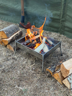 Small metal fire pit with flames and logs on a ground surface