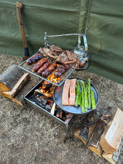 Outdoor cooking setup with grill, asparagus, and bread over a campfire.
